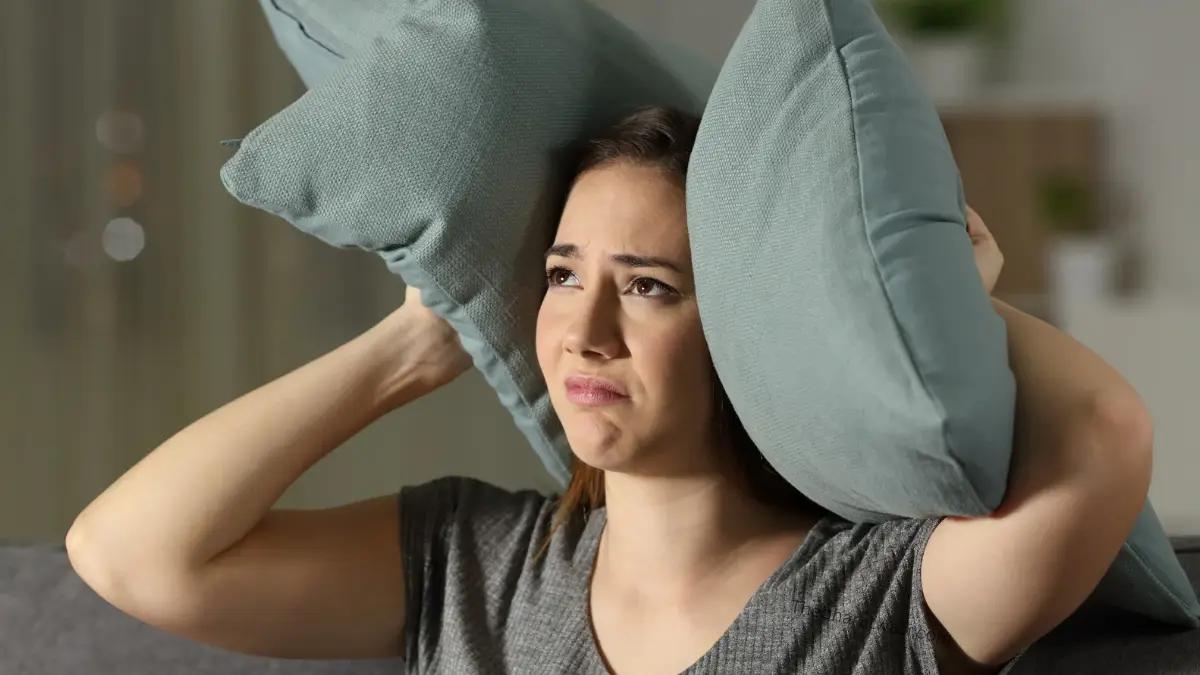 A Young and Beautiful Girl Covering Her Ears By a pillow to reduce the noise created by Neighbours